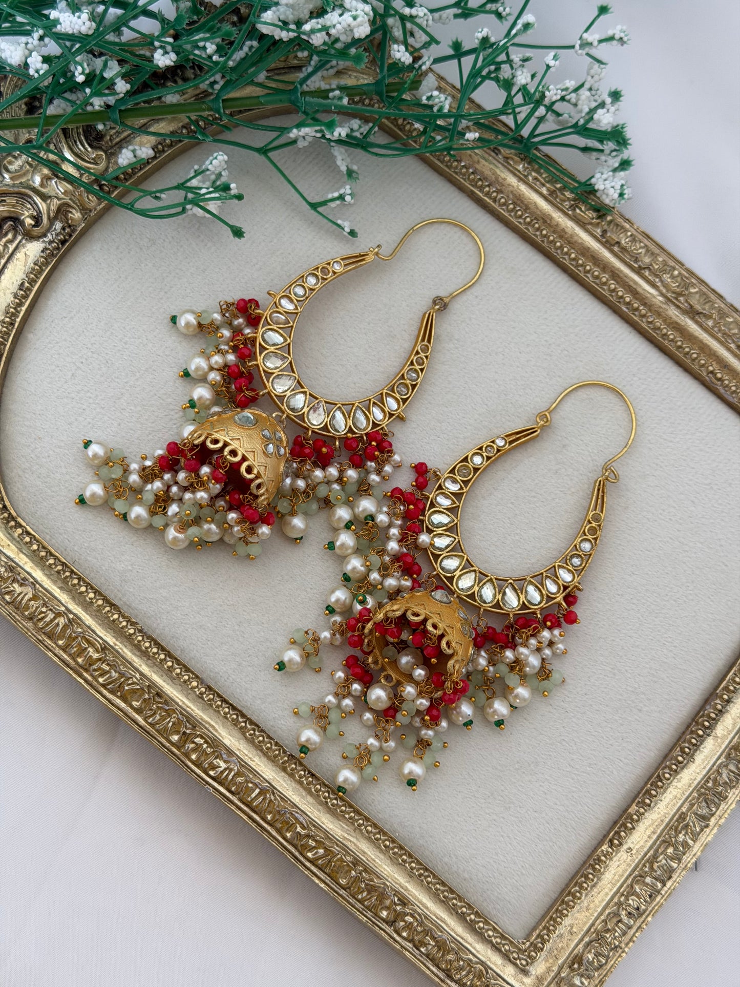 Ornate gold and red earrings on a decorative tray with greenery